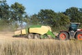 Side view of big modern tractor machine with baler trailer making hay blocks after wheat field harvesting. Agricultural Royalty Free Stock Photo