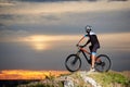 Side view of biker on mountain bike at top of rock restingwit blurred background of the sunset sky Royalty Free Stock Photo