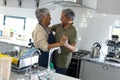 Side view of biracial senior couple holding hands and looking at each other while dancing in kitchen Royalty Free Stock Photo