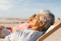 Side view of biracial senior woman sleeping while relaxing on chair with man at beach Royalty Free Stock Photo