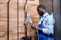 Side view on black repairman handyman in blue overalls holding shower handle in hands