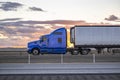 Side view of the blue classic bonnet big rig semi truck with extended cab transporting cargo in refrigerated semi trailer driving Royalty Free Stock Photo