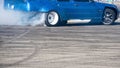 side view of blue sport car drifting on gray speed tarmac track with smoke coming out of the back tire wheel Royalty Free Stock Photo