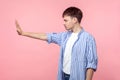 Side view portrait of bossy serious brown-haired man standing with raised palm showing stop gesture. isolated on pink background