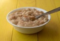 Side view of a bowl of canned chicken dumpling stew in a white bowl with a spoon in the food atop a yellow table