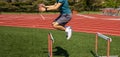 Side view of a boy jumping over a track hurdle