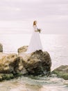 The side view of the bride with the sedding bouquet standing on the stone washed by the sea. Royalty Free Stock Photo