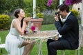 Bridegroom photographing bride blowing kiss while sitting at table in park Royalty Free Stock Photo