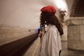 Side view of brunette girl in trench coat and red beret waiting train at metro station Royalty Free Stock Photo