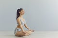 Side view of brunette in lotus position. Woman in yoga meditation, grey background, copy-space.