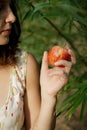 Side view of brunette in summer dress who holding the red apple in the left hand