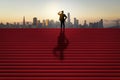 Side view of businessman silhouette looking into the distance on red stairs with shadow and city skyline in the background.