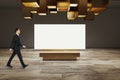 Side view of businessman walking in modern exhibition room interior with creative ceiling lamps, wooden flooring and empty white