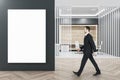 Side view of businessman walking in modern wooden and concrete office interior with blank white mock up poster on wall, furniture Royalty Free Stock Photo