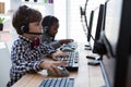 Side view of businessmen using computer while talking through headset at desk Royalty Free Stock Photo