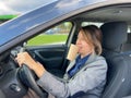 side view of businesswoman driving a car in city with traffic holding cup of coffee in mouth with big eyes looking at Royalty Free Stock Photo