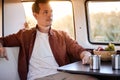 Side View On Calm Male Sitting Behind Table In Mini Van, Looking At Side, Having Rest