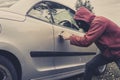 Side view of car being forced by a man in hoodie and mask. Thief tries to steal vehicle from a parking. Young male acts Royalty Free Stock Photo