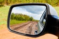 Side view with car rear view mirror on dirty clay road surrounded in natural landscape in a suumer day Royalty Free Stock Photo