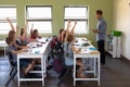 Group of school children sitting at desks and raising their hands to answer Royalty Free Stock Photo