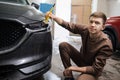 Side view of caucasian man worker of car wash service cleaning headlights of luxury grey car Royalty Free Stock Photo