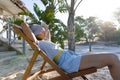 Side view of caucasian young woman wearing hat with hands behind head sitting on deck chair at beach Royalty Free Stock Photo