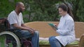 Side view of charming Caucasian doctor endorsing African American handicapped patient in wheelchair talking smiling in