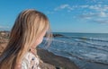 Charming little blond girl relaxing on coastal stones and looking at the sea Royalty Free Stock Photo