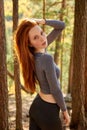 Side view on charming woman with long red hair posing in the forest