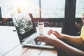 Side view of charming young hipster girl hands working on her laptop sitting at wooden table in a coffee shop. Royalty Free Stock Photo