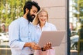 Side view of cheerful bearded business man and young attractive blonde female colleague working on laptop and discuss Royalty Free Stock Photo