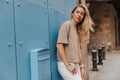 The side view of cheerful blonde woman staying near to wall on the blue background Royalty Free Stock Photo