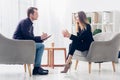 Side view of cheerful businesswoman in suit sitting on armchair and giving interview to journalist Royalty Free Stock Photo