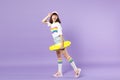 Side view of cheerful teen girl in vivid clothes holding yellow skateboard, looking back isolated on violet pastel Royalty Free Stock Photo