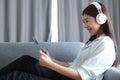 Side view of cheerful woman with headphones lying on sofa using tablet and listening to music. Royalty Free Stock Photo