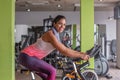 Side view of a cheerful young adult woman in activewear doing cardio on a stationary bike at gym Royalty Free Stock Photo