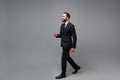 Side view of cheerful young bearded business man in classic black suit shirt tie posing isolated on grey wall background Royalty Free Stock Photo