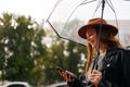 Side view of cheerful young woman wearing elegant hat using typing smartphone smiling looking away standing with Royalty Free Stock Photo