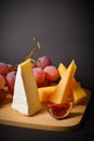 Side view of Cheeseboard platter with hard and soft mould cheese, grape and segmented fig on wooden board