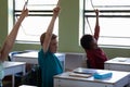 Group of school children sitting at desks and raising their hands to answer Royalty Free Stock Photo