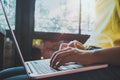 Side view and close-up of charming young hipster girl hands working on her laptop sitting at wooden table in a coffee shop. Royalty Free Stock Photo