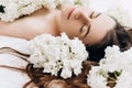 Side view close up portrait of cute millennial girl with fresh spring flowers, lying on cozy bed. Face of young beautiful brunette Royalty Free Stock Photo