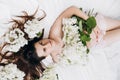 Side view close up portrait of cute millennial lady with fresh spring flowers, lying on comfy bed. Face of young cute caucasian Royalty Free Stock Photo