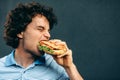 Side view of close-up portrait of young handsome man eating a healthy burger. Hungry man in a fast food restaurant eating a