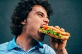 Side view of close-up portrait of young handsome man eating a healthy burger. Hungry man in a fast food restaurant eating a