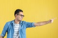 Side-view, close up of young Asian handsome bearded man, wearing eyeglasses, in denim shirt, pointing playfully to his left side, Royalty Free Stock Photo