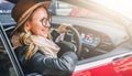 Side view, close up. Young smiling woman in glasses and hat sits behind wheel in red car. Trip, caravanning, tourism. Royalty Free Stock Photo