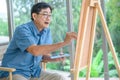 Side view of concentrated senior man painting picture on easel at home Royalty Free Stock Photo