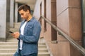 Side view of confident handsome young man using mobile phone standing on stairs of modern office building. Royalty Free Stock Photo