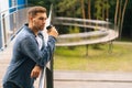 Side view of confident thoughtful young man standing on balcony terrace and drinking coffee leaning on railing of office Royalty Free Stock Photo